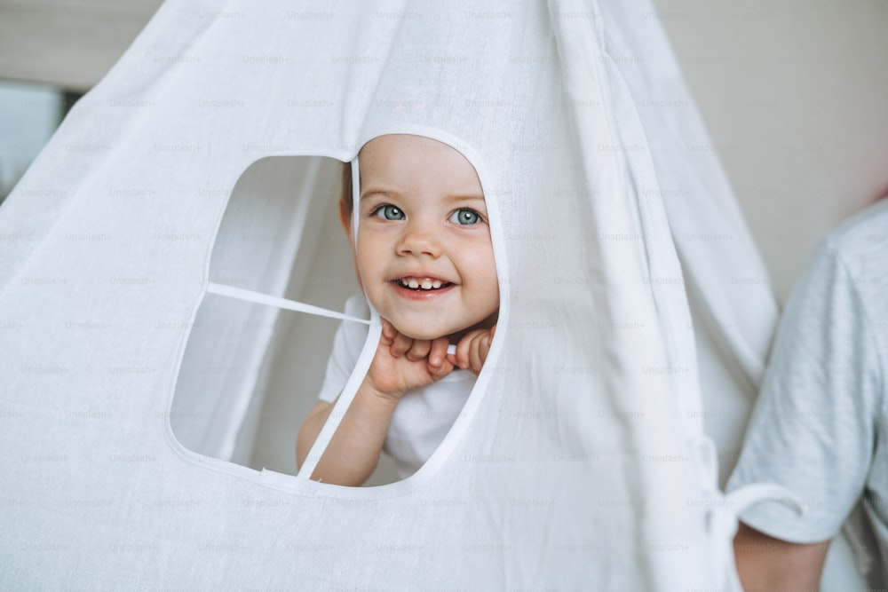 Cute funny baby girl having fun in wigwam in children room at home