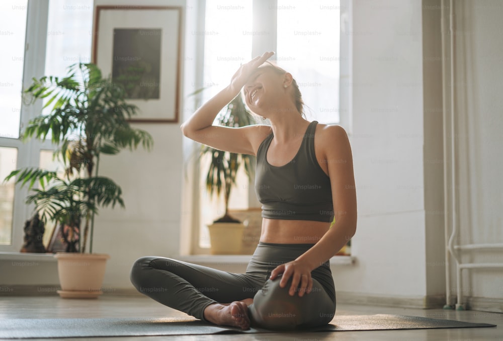 La giovane donna in forma pratica lo yoga nello studio di yoga leggero con la pianta della serra