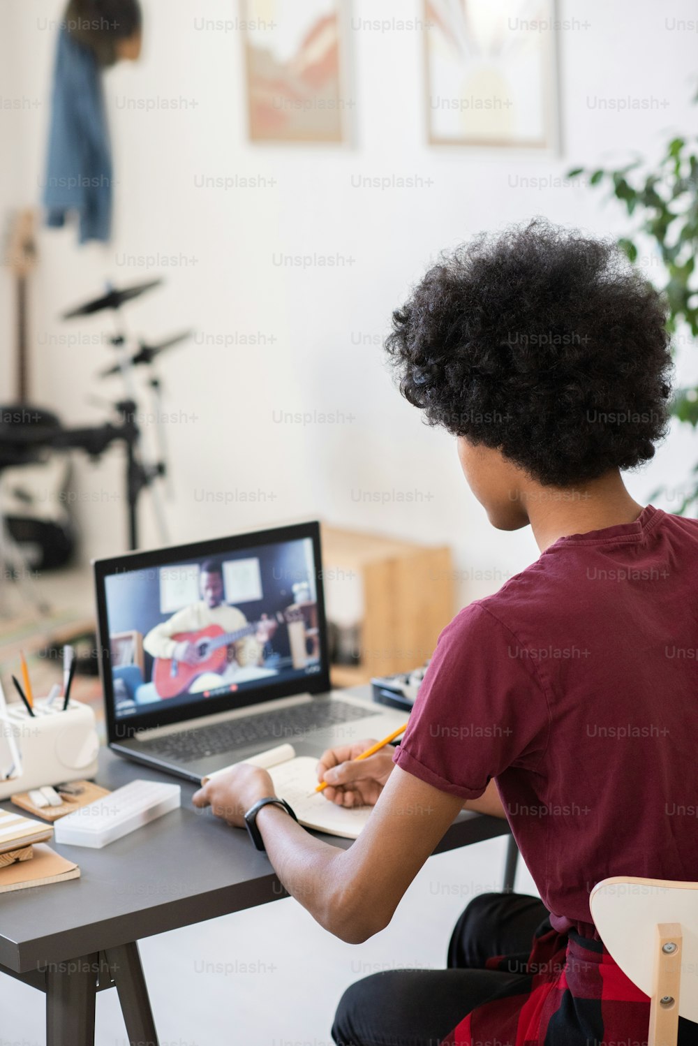 Biracial guy making notes while sitting by table and looking at music teacher with guitar on laptop screen