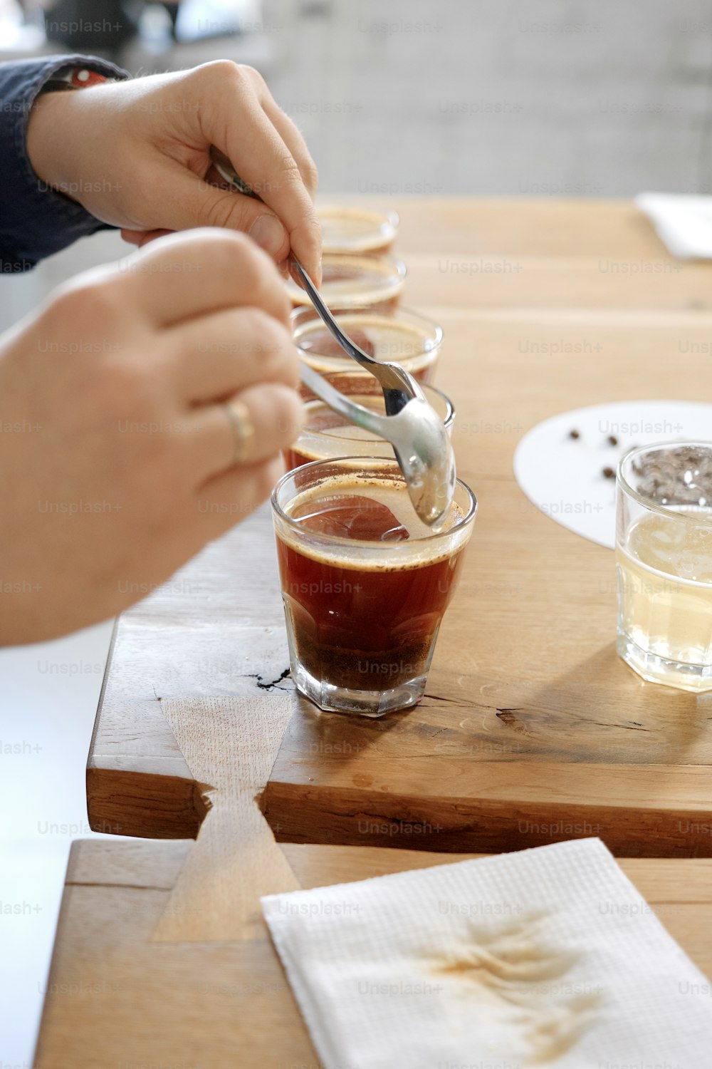 Primo piano delle mani dell'uomo che assaggiano il caffè appena preparato in tazza di vetro, usando il cucchiaio, esaminando il gusto e il sapore del caffè alla prova di coppettazione del caffè per barosta