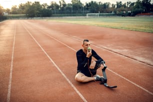 Un corredor con pierna protésica relajándose con música y comiendo manzana en el estadio.