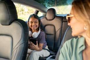 Hija feliz mirando a su madre mientras está sentada en el asiento trasero dentro de un coche eléctrico