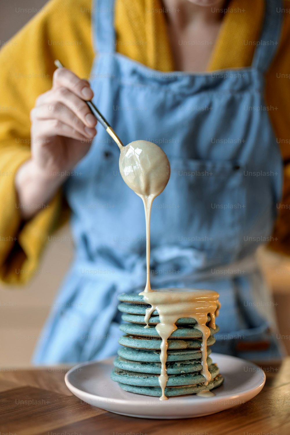 Donna in grembiule blu che versa frittelle blu con zuppa di caramello sul tavolo di legno. Cibo gustoso fatto in casa. Celebrazione del Carnevale.