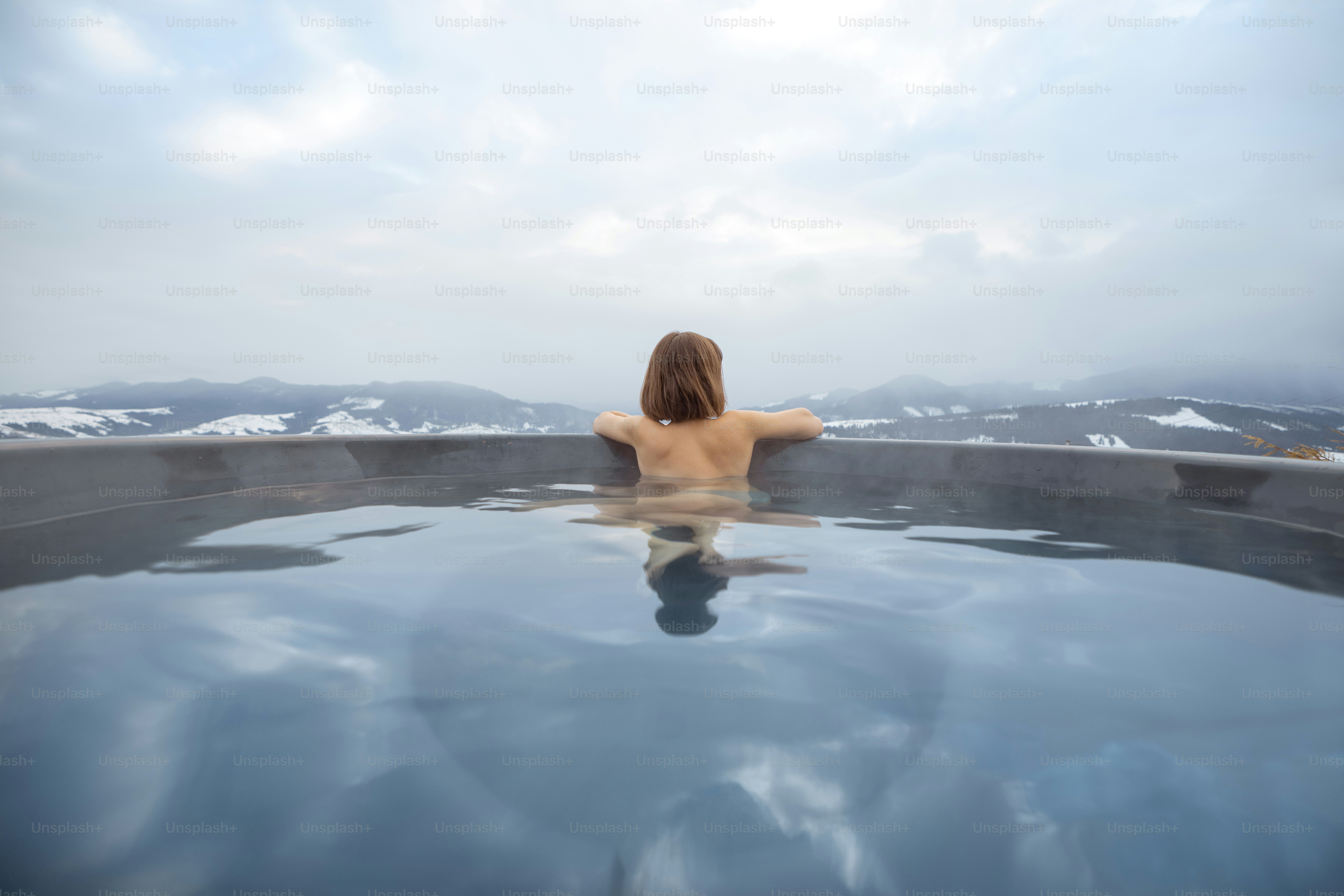 Young woman bathing in hot tub at mountains during winter. Concept of rest and recovery in hot vat on nature. Idea of escape and recreation on mountains