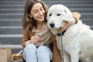 Pretty woman have outdoor lunch near office building with her big white dog while sitting on the stairs, hugs her dog. Pet friendly and pet care concept. Animal lover.