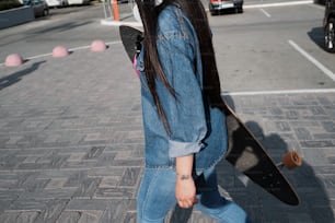 Close up of a girl in denim wear holding a longboard while crossing the road.
