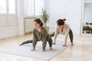 Attractive mother middle age woman and daughter teenager ptactice yoga together in the bright room