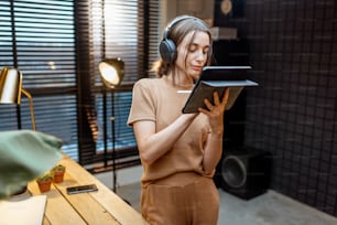 Junge und kreative Frau kreiert auf einem digitalen Tablet Musik in Kopfhörern im modernen Heimstudio