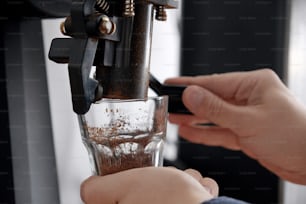 Close up of man using coffee machine, grinding coffee beans into cups, preparing for coffee brewing examination
