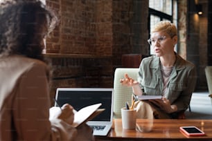 Zwei junge Geschäftsfrauen beraten bei einem Meeting, während eine von ihnen Notizen macht