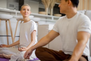 Multiracial couple practising yoga and meditating while sitting on fitness mats at home. Concept of healthy lifestyle. Idea of domestic hobby and leisure. Asian man and caucasian girl with closed eyes