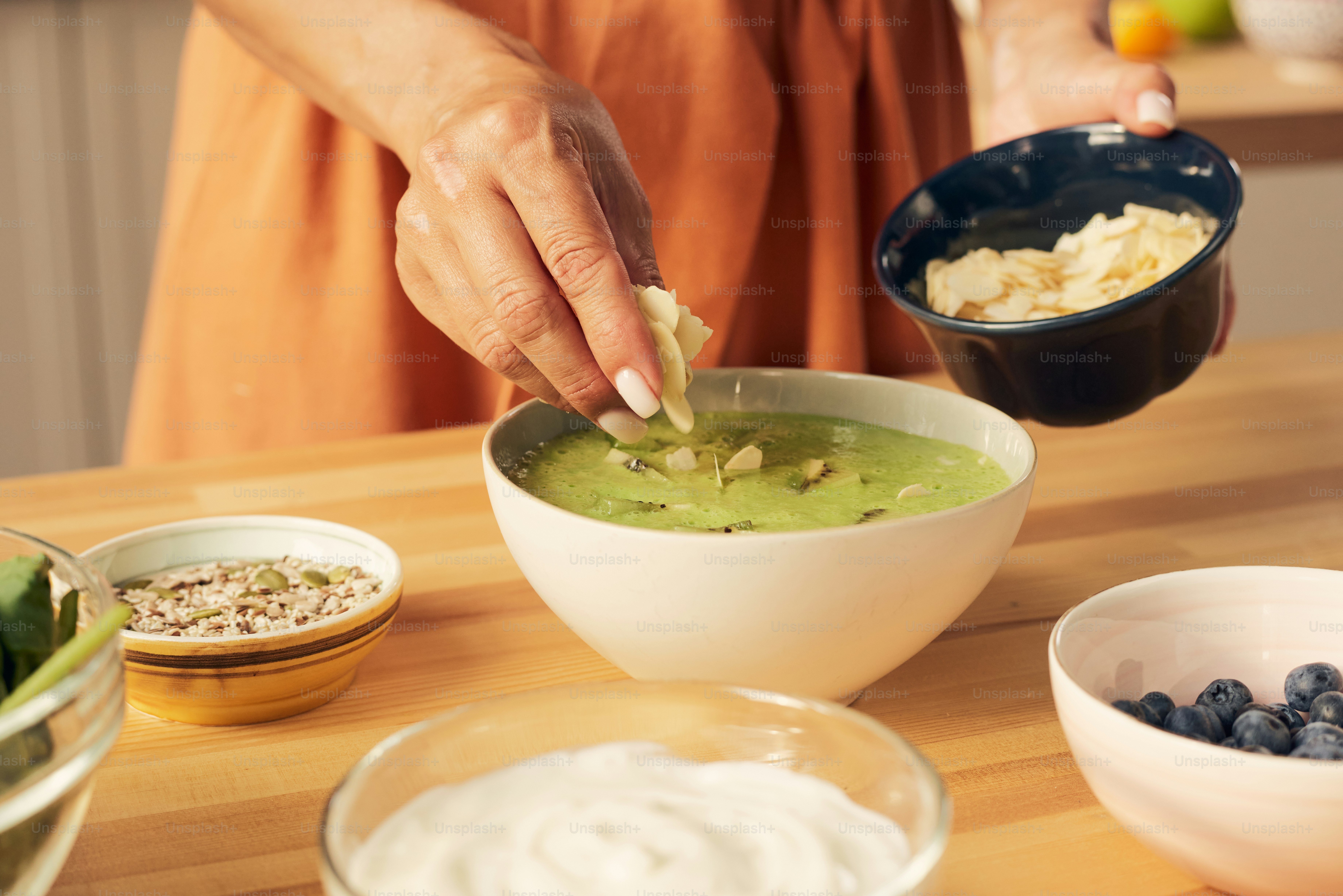 Hand of female decorating fresh homemade green smoothie with almond flakes by table before serving it for breakfast