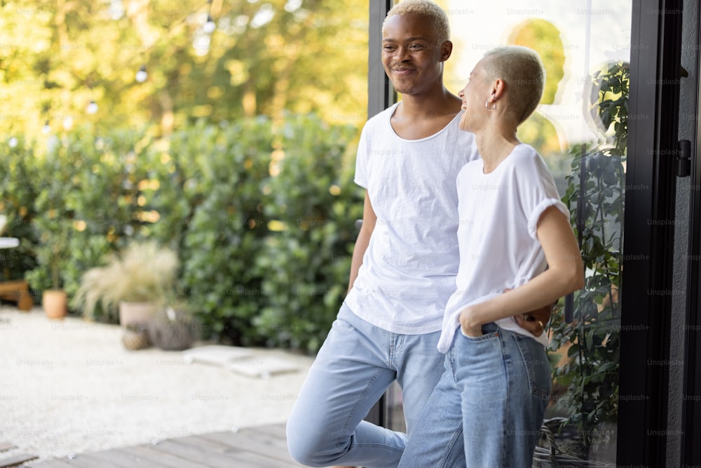 Multiracial couple standing and resting together on home terrace. Concept of relationship. Modern domestic lifestyle. Black man and european girl enjoying time together. Sunny daytime
