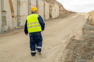 Rear view of contemporary quarry worker moving down road along unfinished wall of construction