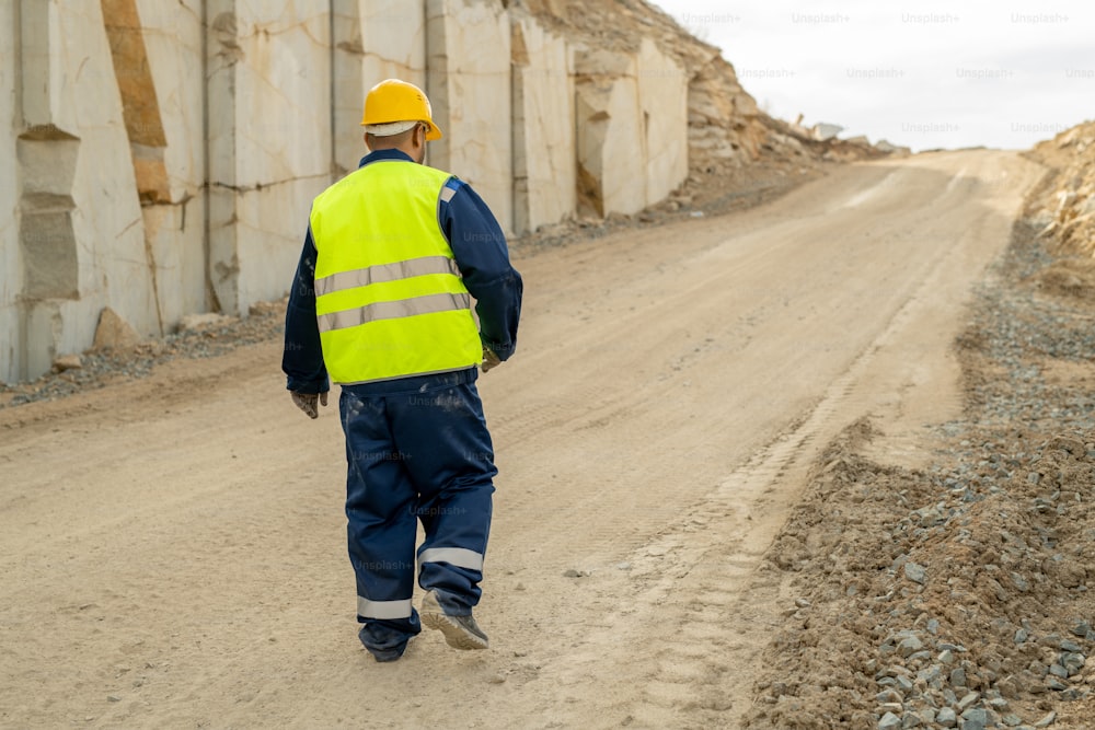 Rear view of contemporary quarry worker moving down road along unfinished wall of construction