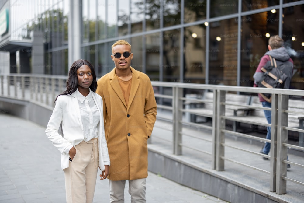 Latin man and african woman walking on city street and talking. Concept of remote and freelance work. Idea of business cooperation. Smiling businesswoman and businessman wearing formal wear