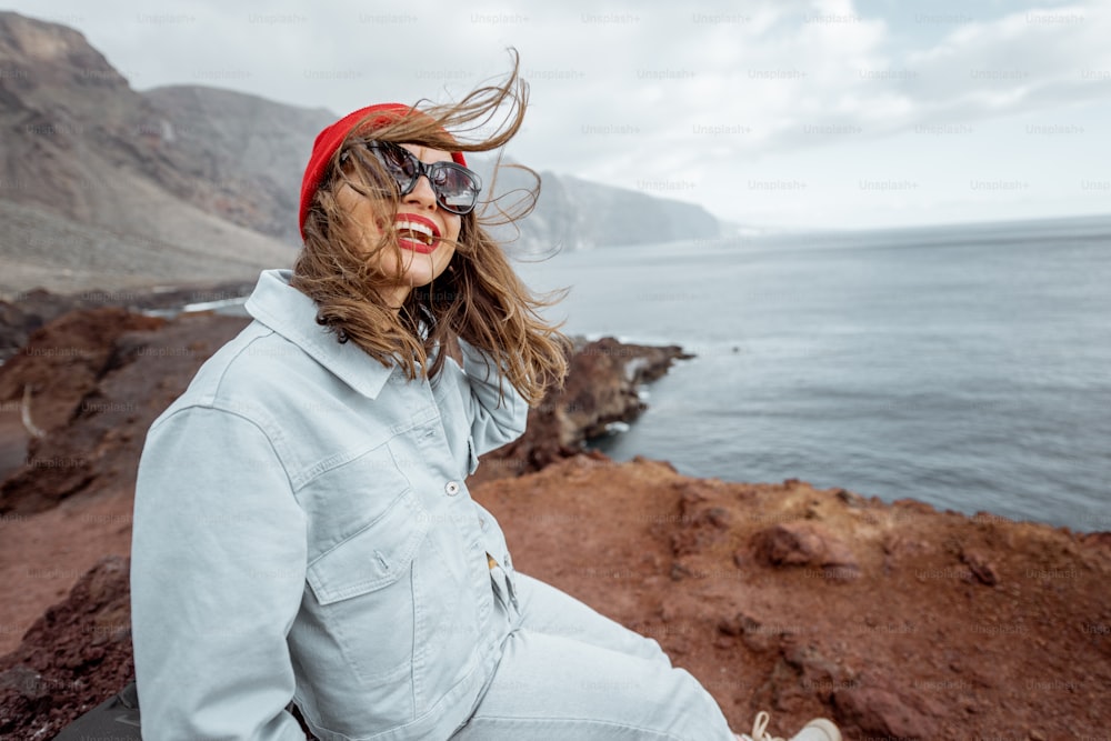 Retrato de estilo de vida de una mujer elegante que disfruta de un viaje en una costa rocosa del océano durante un viento fuerte. Viajar por la isla de Tenerife, España