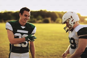 Two smiling young American football players standing on a field and talking together after a team practice in the late afternoon
