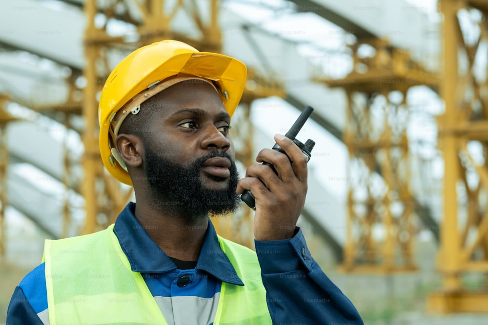 Afrikanischer Bauarbeiter im Arbeitshelm spricht im Sender bei der Arbeit auf der Baustelle im Freien