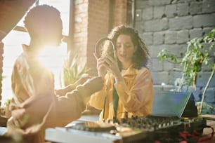Junge Frau in Freizeitkleidung mit Kopfhörern, während sie mit ihrem afroamerikanischen Freund in einer Loft-Wohnung neue Musik kreiert