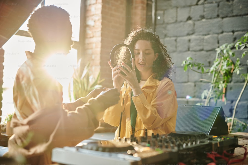 Mujer joven en ropa informal sosteniendo auriculares mientras crea nueva música con su novio afroamericano en un apartamento tipo loft