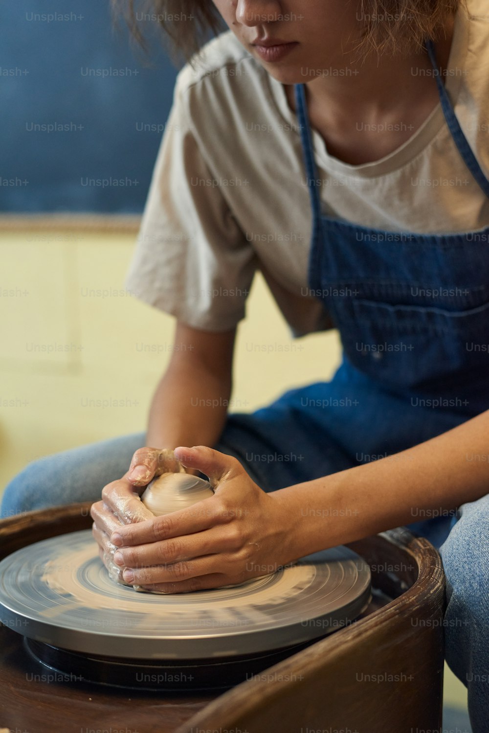 エプロンで真面目な女の子の接写は、ワークショップで糸車にそれを形作りながら粘土に手をつないでいます