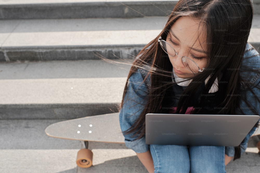 Student in jeans and denim jacket typing on the laptop standing on her knees.