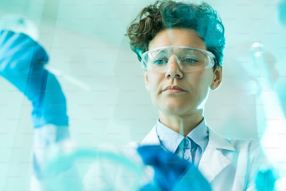 Unten Ansicht einer konzentrierten Forscherin mit Schutzbrillen bei der Arbeit mit Proben im Labor