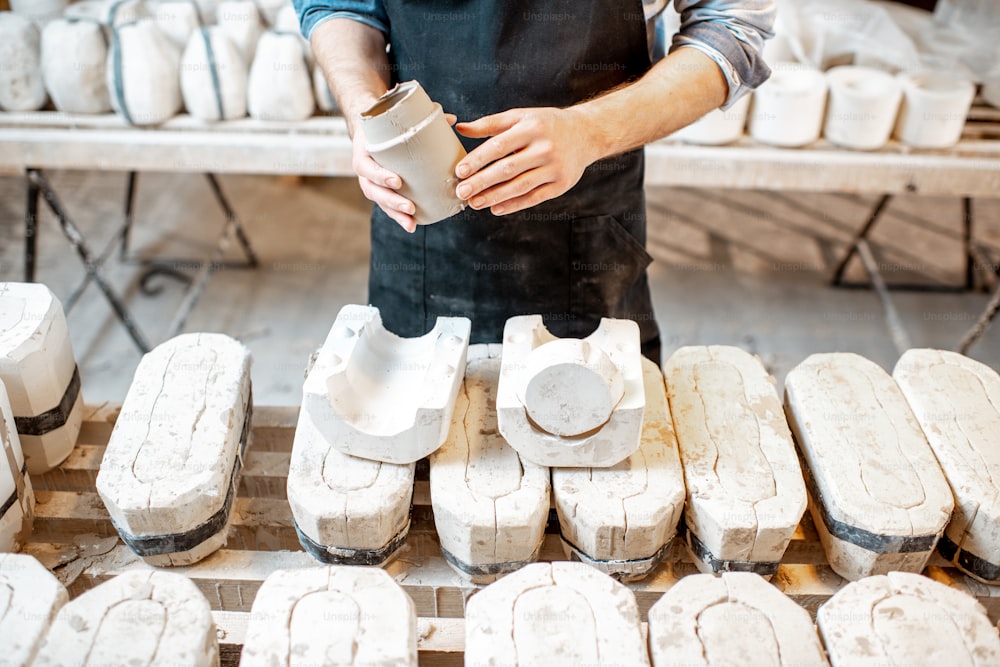 Male worker getting clay products from the gypsum forms at the pottery manufacturing, close-up view