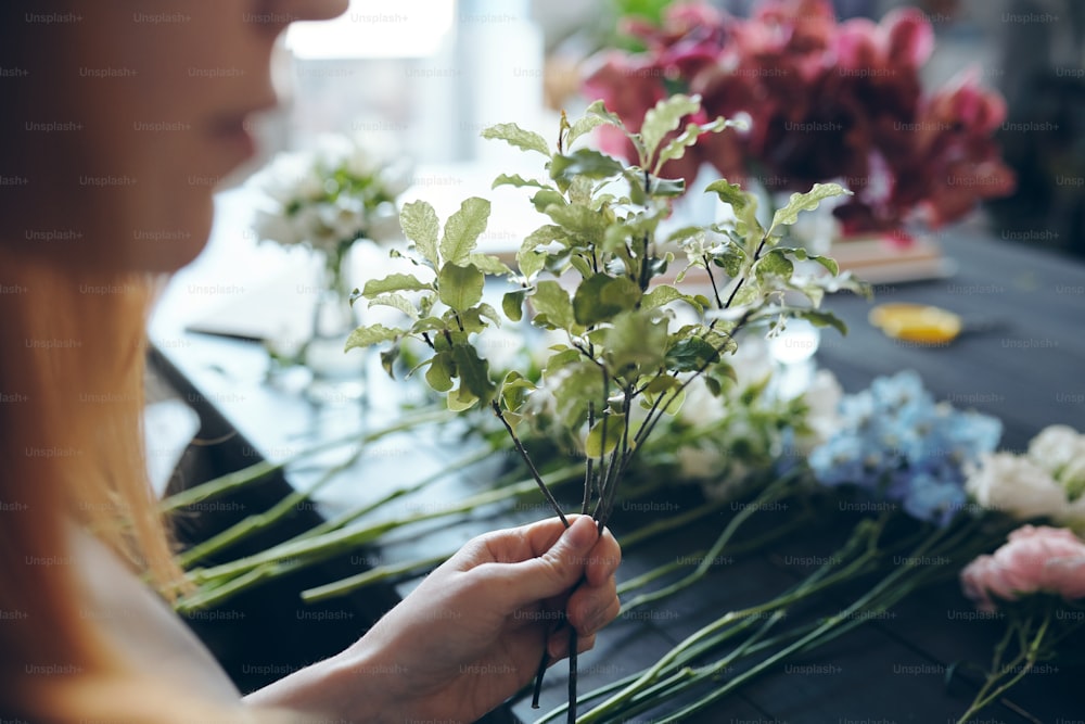 꽃집이 카운터에 서서 꽃을 줄지어 놓고 질감을 위해 꽃다발에 녹지를 추가하는 클로즈업