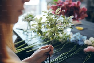 꽃집이 카운터에 서서 꽃을 줄지어 놓고 질감을 위해 꽃다발에 녹지를 �추가하는 클로즈업