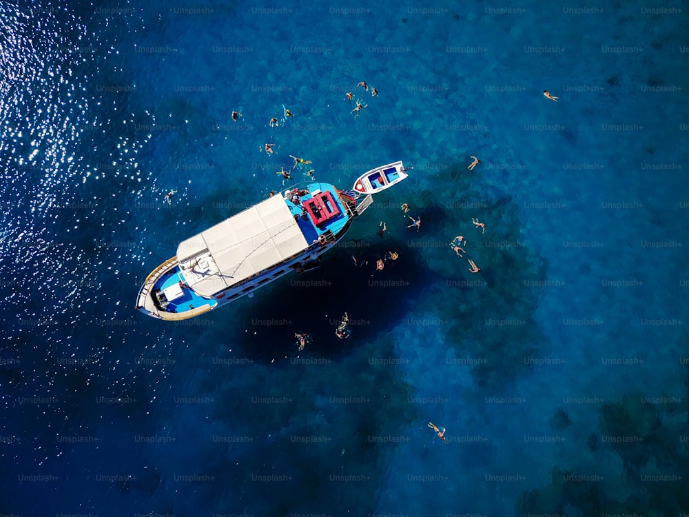 Aerial shot of beautiful blue lagoon at hot summer day with sailing boat. Top view of people are swimming around the boat.