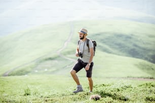 Man hiking with backpack on the beautiful green meadow while traveling in the mountains during the sunny weather