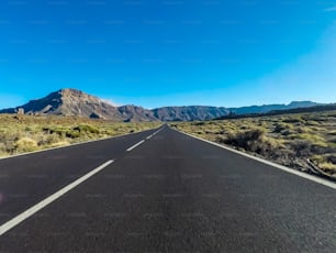 Camino largo en la montaña con montura vulcana en el frente y cielo azul claro - punto de vista del suelo con asfalto negro y líneas blancas - concepto de conducción y viaje