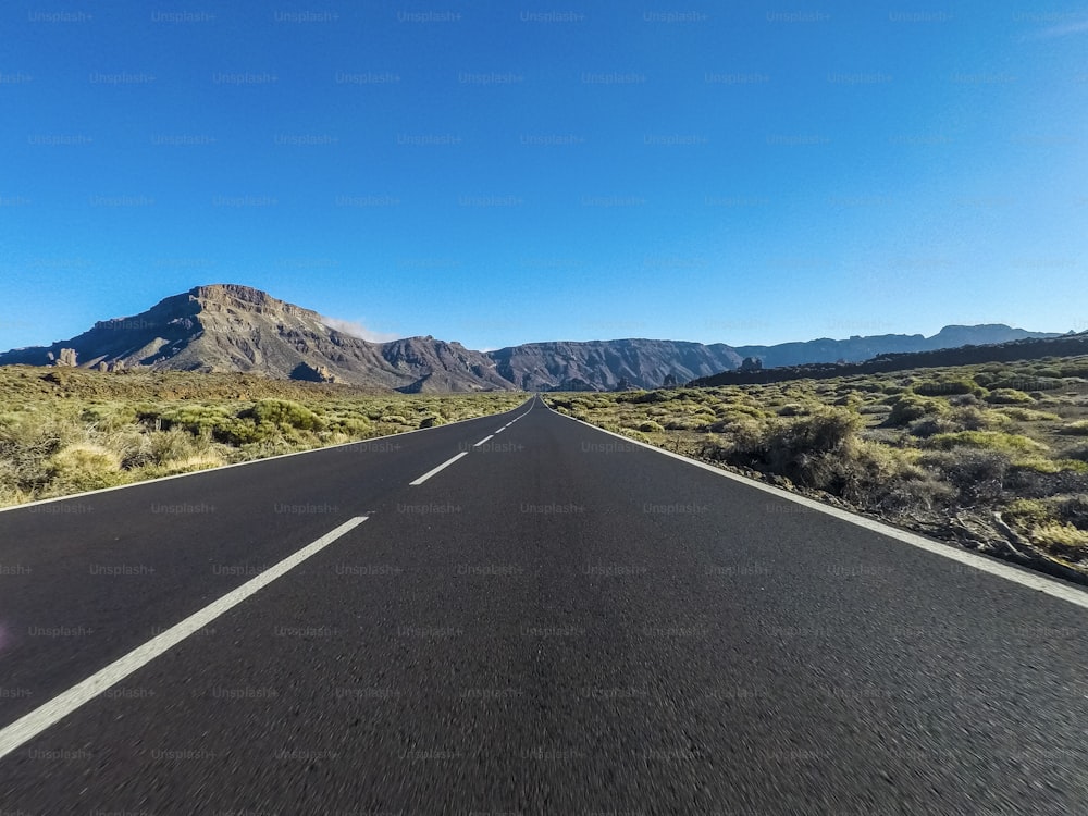 バルカンマウントが正面にあり、青く澄んだ空がある山の長い道のり - 黒いアスファルトと白い線で地面の視点 - 運転と旅行のコンセプト