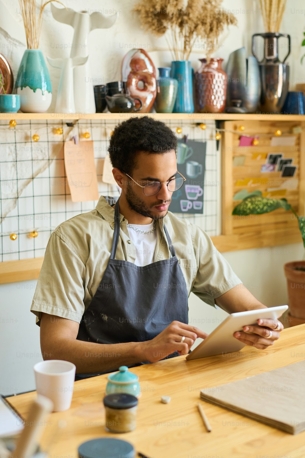 Serious guy in casualwear and apron looking at screen of digital tablet while scrolling through online information and creative ideas