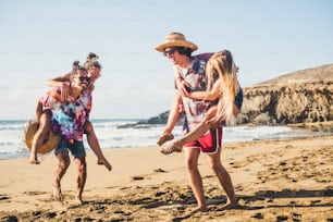 행복한 젊은이들은 함께 즐거운 시간을 보낸다 - 젊은 남녀 그룹이 해변에서 여름 휴가 휴가를 즐긴다 - 남자들은 화창한 날에 여자를 어깨에 메고 있다 - 배경의 바다 - 관광 개념
