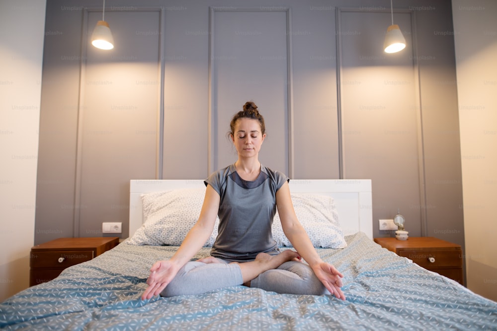 Attractive shape sporty middle aged woman doing seated yoga poses on the bed before sleeping.