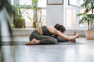 Jeune femme en forme pratique le yoga en faisant des asanas dans un studio de yoga léger avec une plante d’intérieur verte