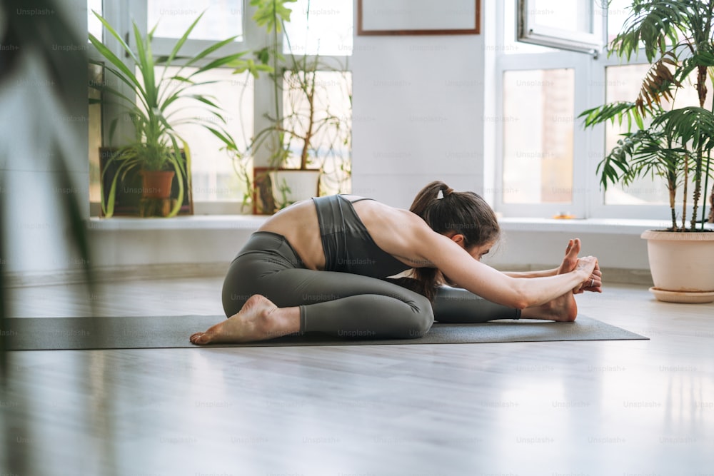 Mulher jovem em forma pratica yoga fazendo asana no estúdio de yoga leve com planta da casa verde