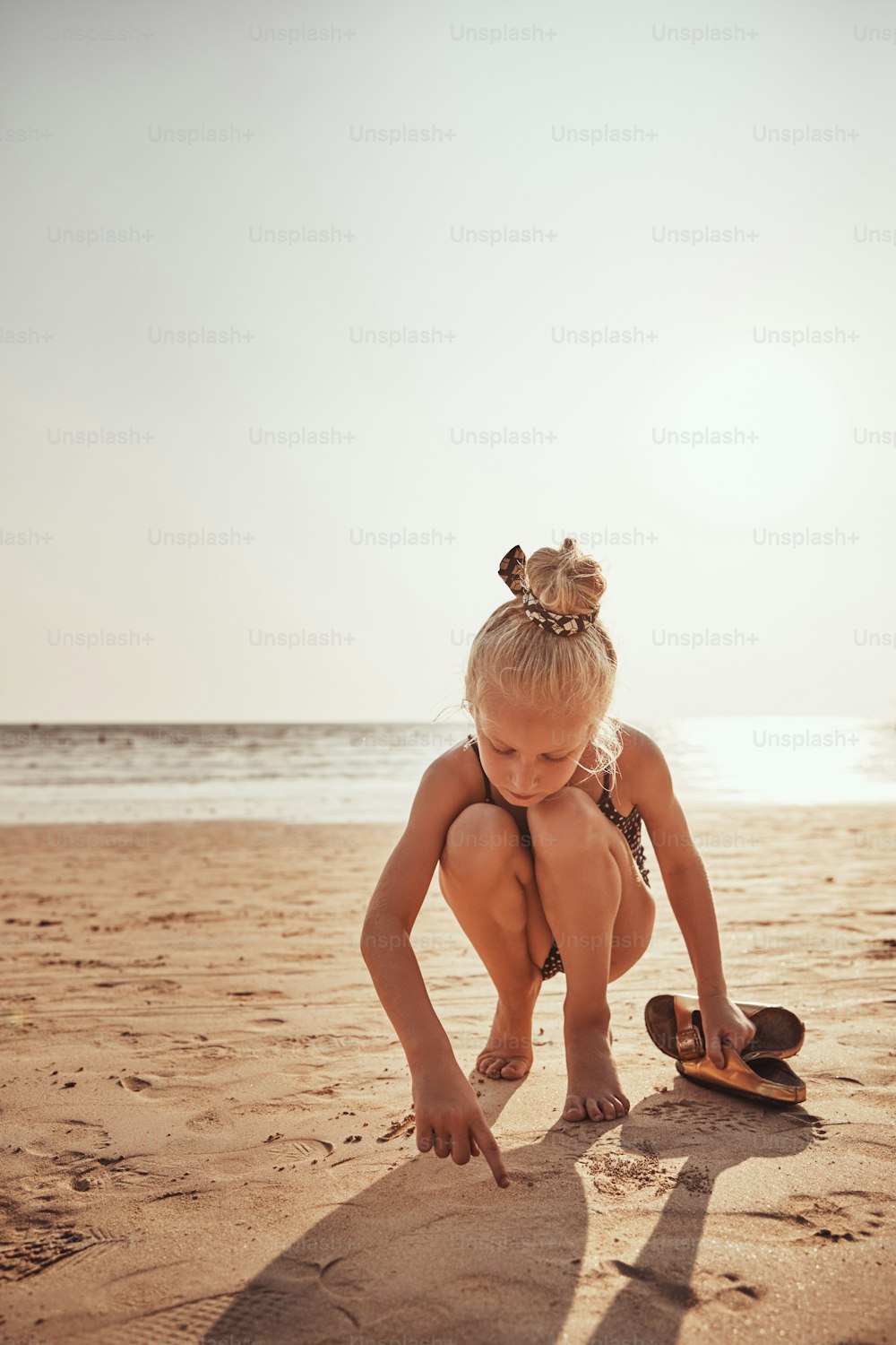 Little girl in green bathing suit plays in sand on beach, green