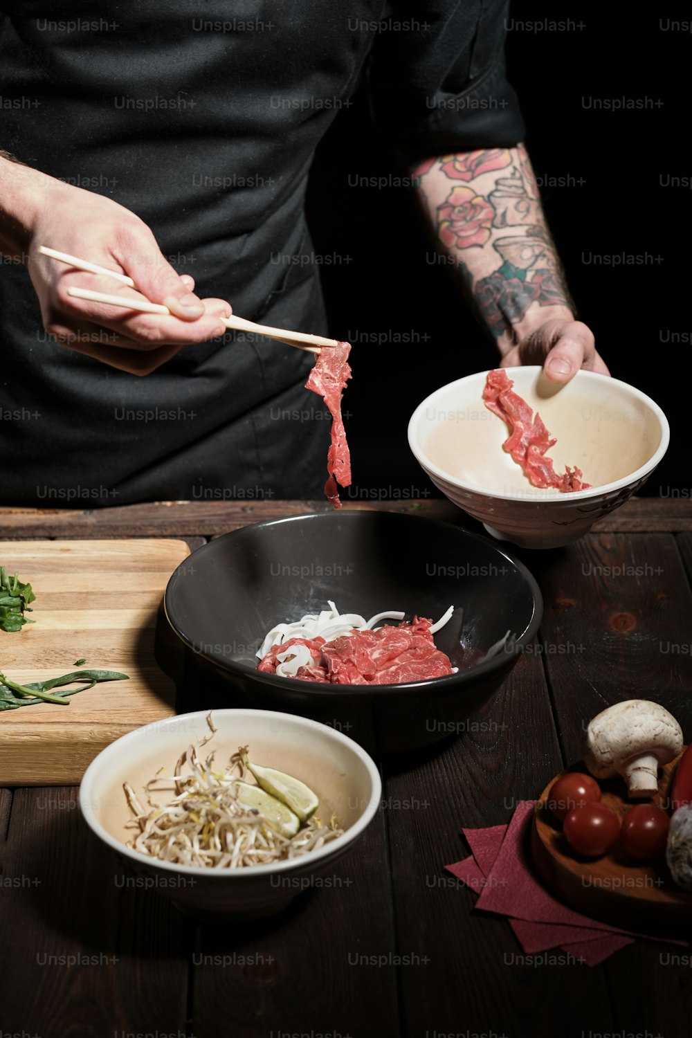 Close up of chef's hands adding beef to noodle bolw with chopsticks