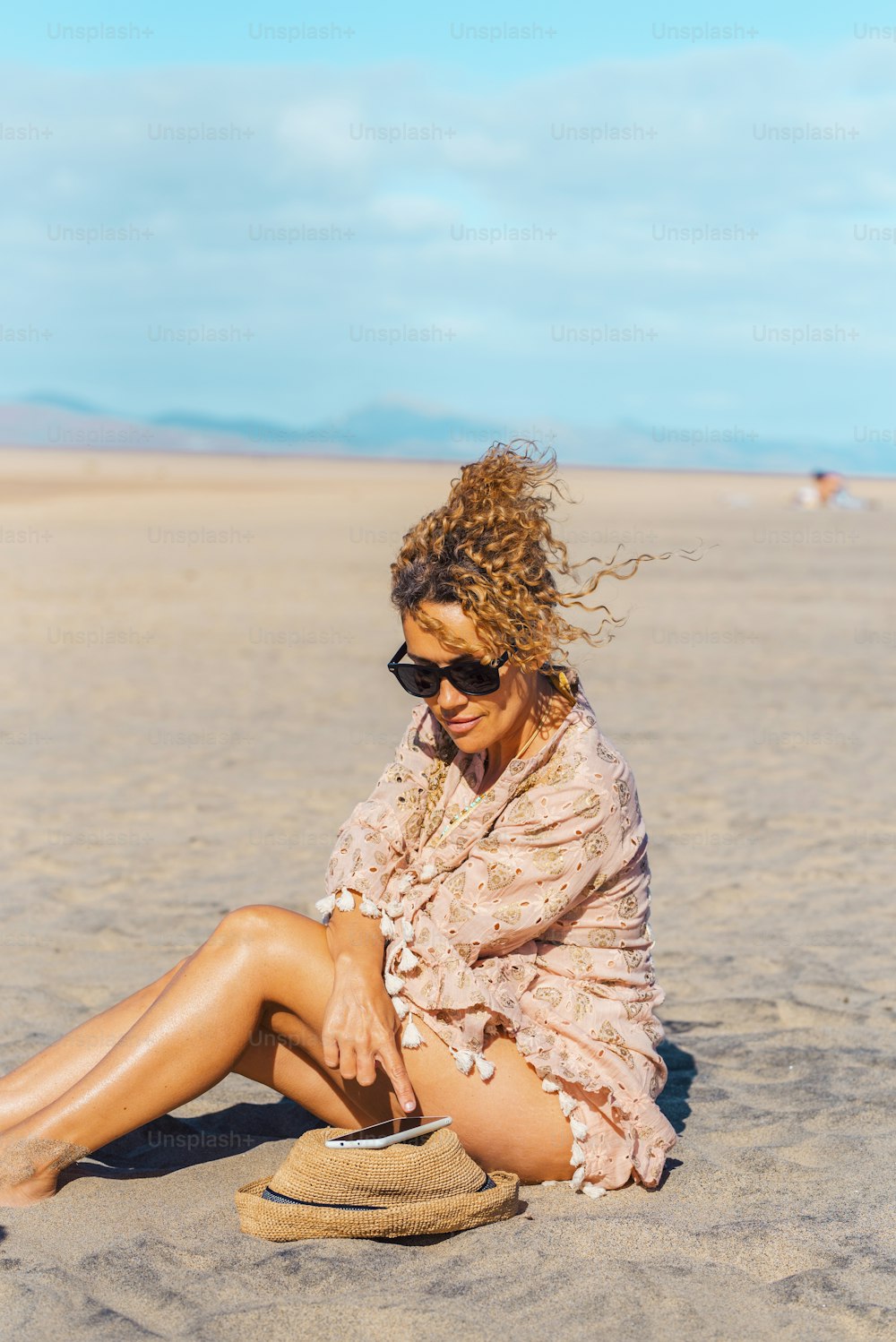 Turista femenina se relaja bajo el sol en el día de vacaciones de verano en la playa usando el teléfono móvil. La mujer adulta atractiva disfruta de la conexión al aire libre. Gratis mujer soltera en solitario personas en actividad turística