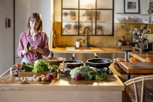 Junge Frau mischt Salat, während sie zu Hause in der Küche gesundes Essen kocht. Gesunder Lebensstil und Wellnesskonzept. Idee des Veganismus