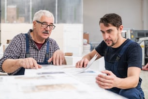 Concentrated senior and young workers sitting at stack of pages and examining printed papers