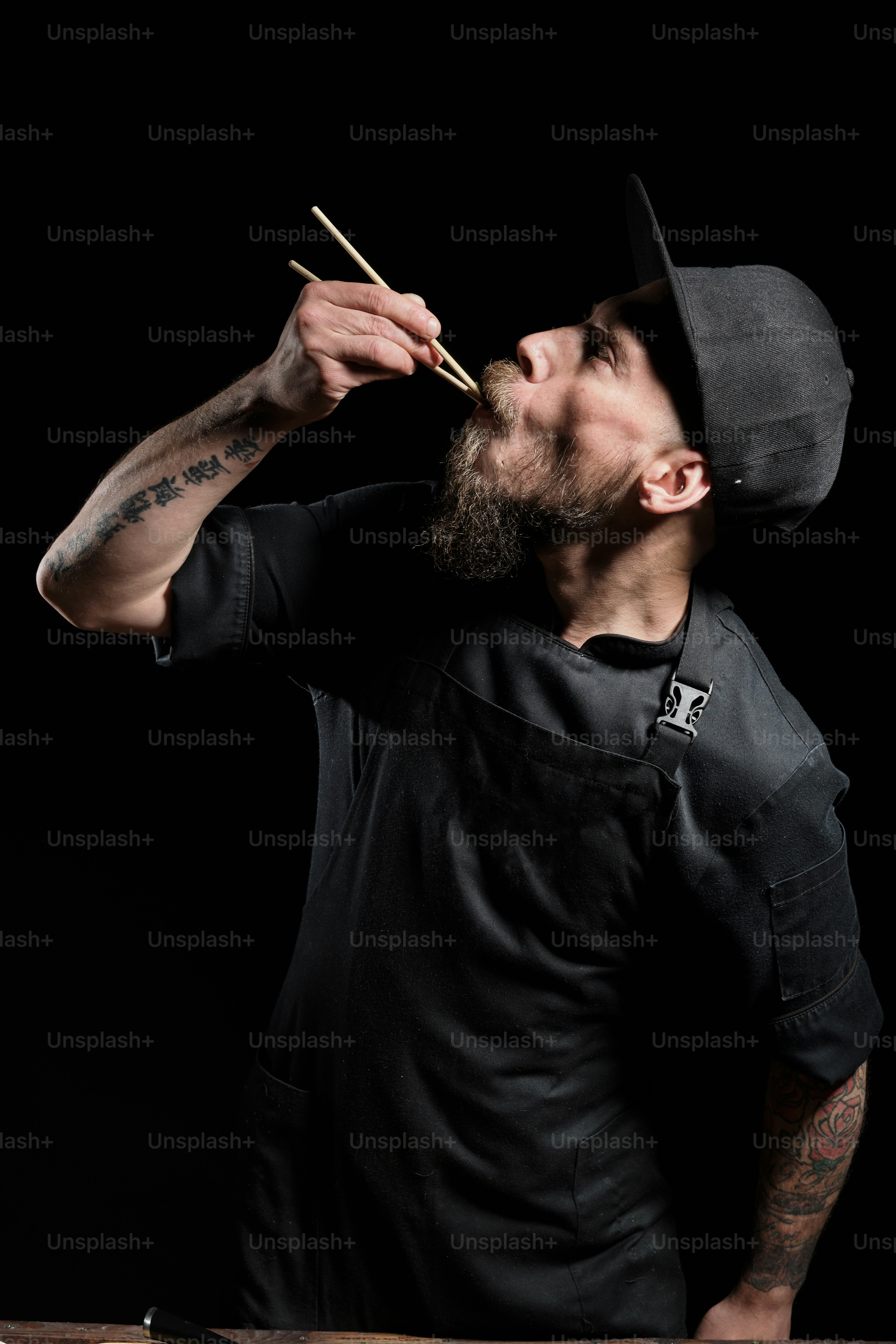 Portrait of brutal male chef in studio tasting food with chopsticks