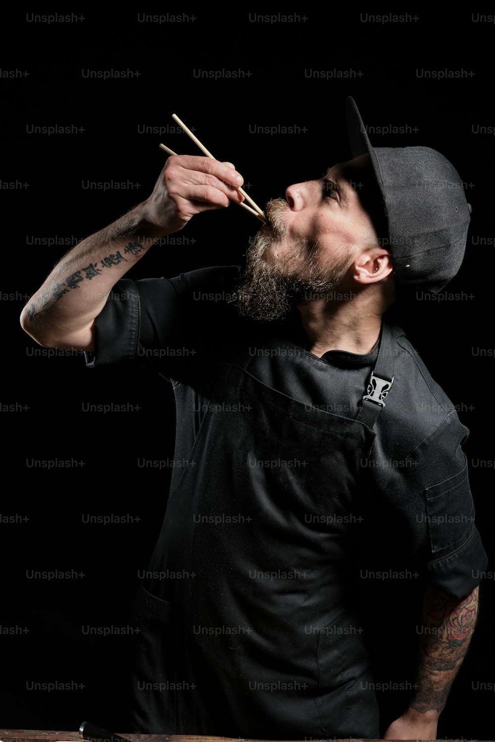 Porträt eines brutalen männlichen Kochs im Studio, der Essen mit Essstäbchen probiert