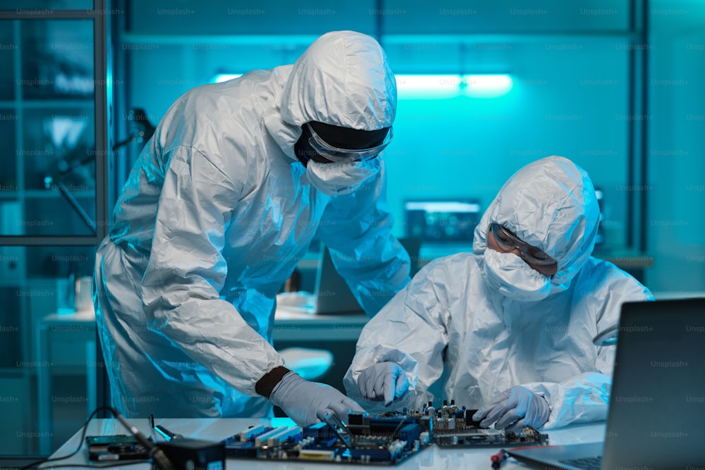 Two contemporary lab workers in protective coveralls consulting about repairment of motherboard or microprocessor