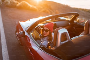 Mulher nova que viaja de carro em uma bela estrada da montanha durante um pôr do sol