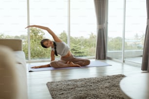 Yoga fitness. Menina treinando, alongando o corpo em casa pela manhã. Mulher asiática bonita com corpo apto em roupas esportivas pratica pose de yoga no tapete na sala de estar